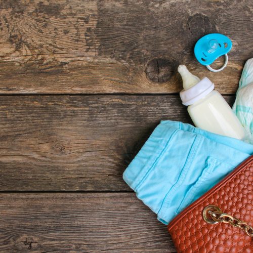 Women's handbag with items to care for the child on old wooden background
