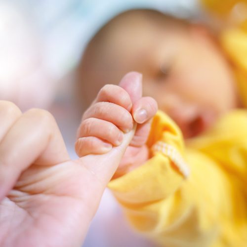 Newborn baby touching his mother hand, Baby holding finger of his mother giving senses of attachment and bonding. The image taken with a selective focus stressing an emotional scene.